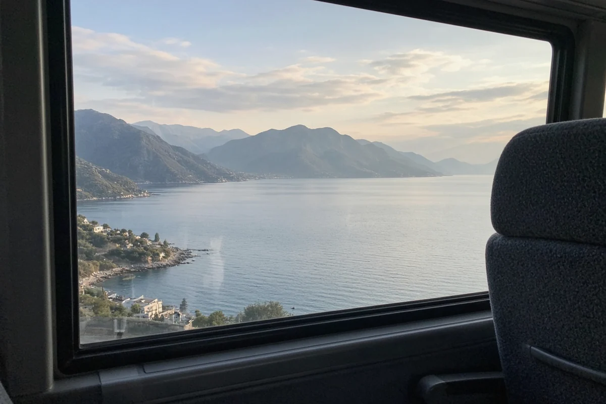 A calm mountain-ringed bay seen through a coach window, with a seat back in the foreground